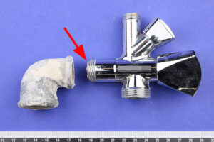 Das Kombi-Eckventil und das Winkelfitting werden im Labor untersucht. Das Anschlussgewinde des Ventils ist vollständig umlaufend gebrochen (Pfeil).