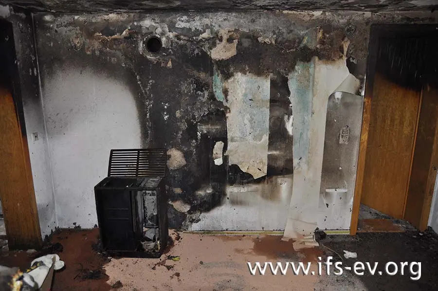 An der Wand ist ein Brandtrichter zu erkennen, an dessen Fußpunkt der Ölofen steht.
