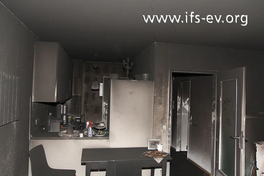 Blick vom Wohnraum in die offene Küche und in den Flur; die ganze Wohnung ist sehr stark durch Ruß verunreinigt.