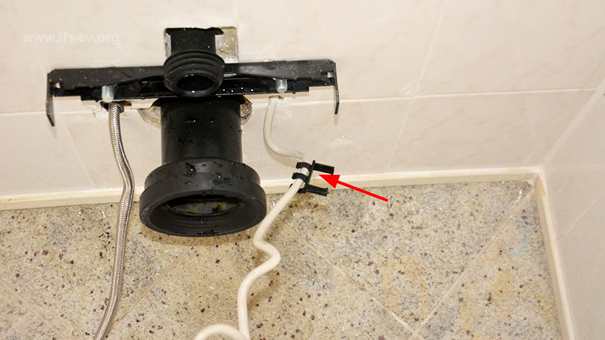 Nach Demontage des WC. Am Kabel ist die Kunststoffführung vorhanden (Pfeil), am Schlauch fehlt diese.
